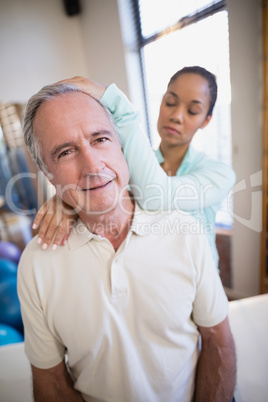 Portrait of senior male patient receiving neck massage from female therapist