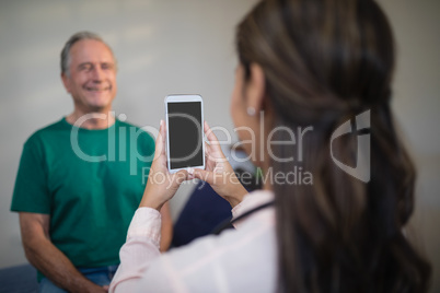 Rear view of female therapist photographing senior male patient from mobile phone