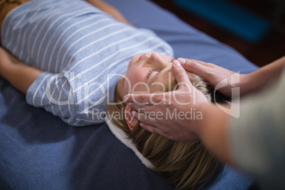 High angle view of female therapist giving head massage to boy lying on bed