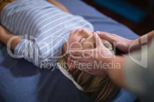 High angle view of female therapist giving head massage to boy lying on bed