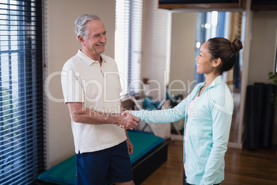 Smiling senior male patient shaking hands with female therapist