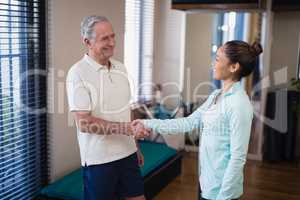 Smiling senior male patient shaking hands with female therapist