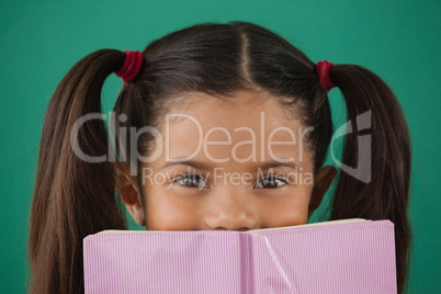 Schoolgirl hiding behind a book against green background