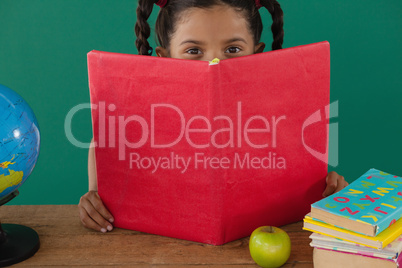 Schoolgirl hiding behind a book against green background