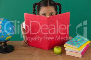 Schoolgirl hiding behind a book against green background