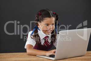 Schoolgirl using laptop against blackboard