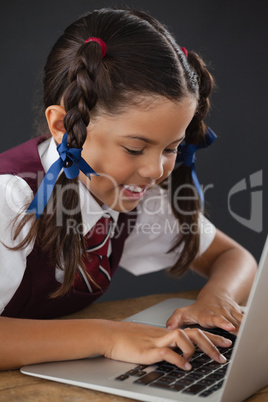 Schoolgirl using laptop against blackboard