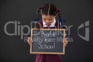 Schoolgirl holding slate with text against blackboard