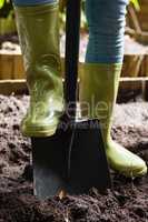 Low section of woman standing with shovel on dirt