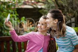 Smiling daughter taking selfie with mother sitting on bench