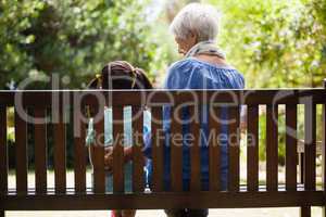 Rear view of granddaughter and grandmother sitting on wooden bench