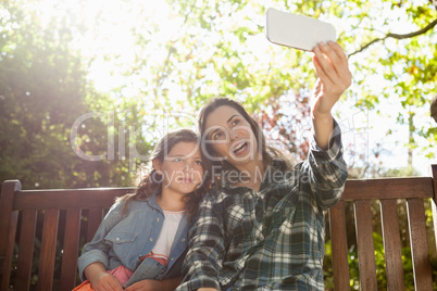 Happy mother taking selfie with daughter while sitting on wooden bench