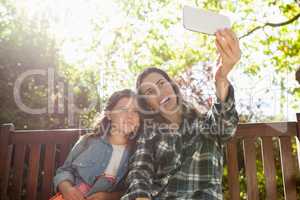 Happy mother taking selfie with daughter while sitting on wooden bench
