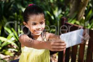 Smiling girl taking selfie while sitting on wooden bench