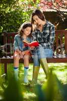 Mother reading book to daughter while sitting on wooden bench