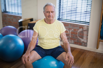 High angle view of senior male patient sitting on exercise ball with eyes closed