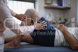 Midsection of female therapist measuring knee while senior male patient lying on bed