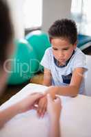 Boy looking while female therapist massaging hand at table