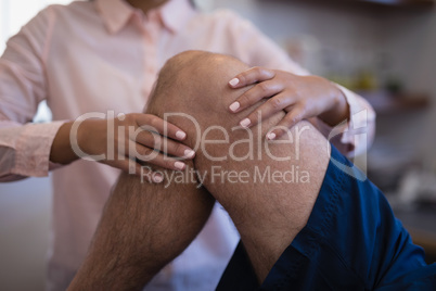 Midsection of female therapist examining knee with senior male patient
