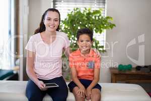 Portrait of smiling female therapist holding digital sitting with arm around boy on bed