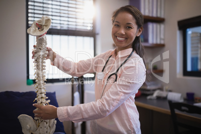 Portrait of smiling young female therapist examining artificial spine on bed