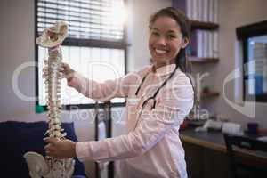Portrait of smiling young female therapist examining artificial spine on bed