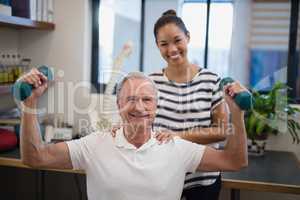 Portrait of smiling female doctor standing with male patient lifting dumbbells