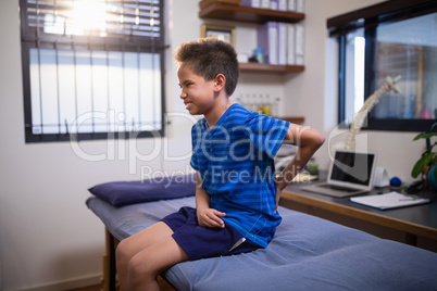 Boy frowning with backache while sitting on bed