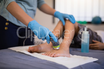 Female therapist wearing gloves scanning feet of boy lying on bed