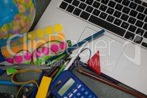 Various school supplies and laptop on chalkboard