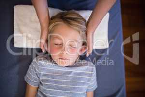 Overhead view of boy with eyes closed receiving neck massage from female therapist