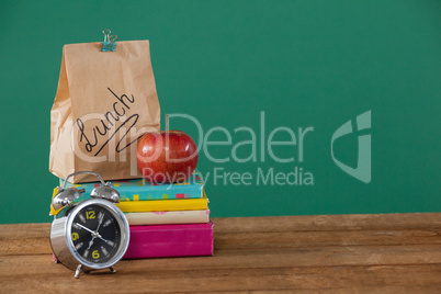 Alarm clock, lunch paper bag and apple on books stack