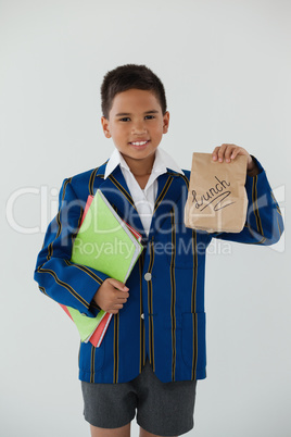 Schoolboy holding books and disposable lunch bag against white background
