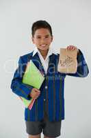 Schoolboy holding books and disposable lunch bag against white background