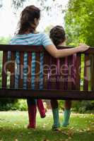 Rear view of girl and woman sitting on wooden bench