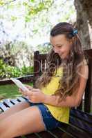 Smiling girl using mobile phone while sitting on wooden bench