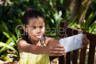Girl sticking out tongue while taking selfie on wooden bench