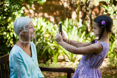 Side view of smiling girl photographing grandmother