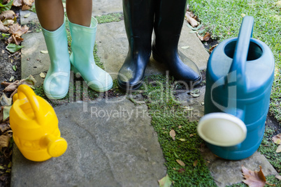 Low section of senior woman and granddaughter standing by watering cans on walkway