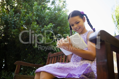 Low angle view of smiling girl using digital tablet while sitting on wooden bench