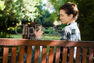 Smiling mother and daughter sitting on wooden bench