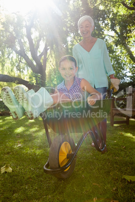 Smiling grandmother pushing granddaughter in wheelbarrow