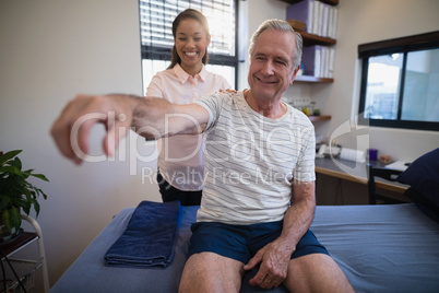 Smiling female doctor examining shoulder of senior male patient