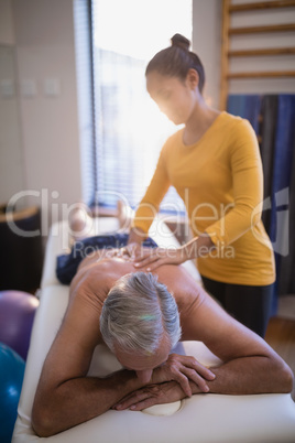 Female therapist massaging back of senior male patient against window