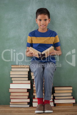 Schoolboy sitting on books stack and reading book