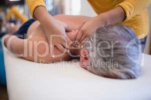 Shirtless senior male patient lying on bed receiving neck massage from female therapist