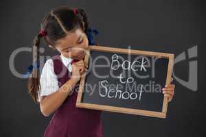 Schoolgirl holding slate with text against blackboard