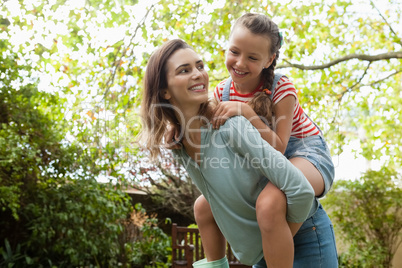 Cheerful mother giving daughter piggyback ride against trees