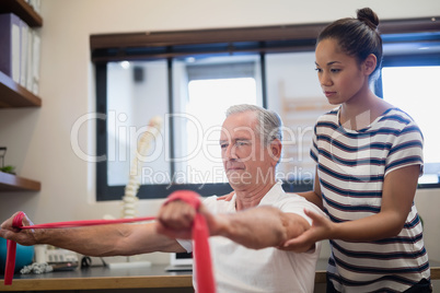 Female doctor looking at male patient pulling red resistance band