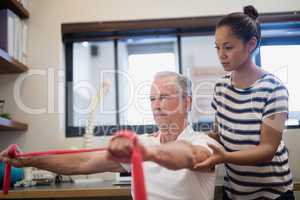 Female doctor looking at male patient pulling red resistance band
